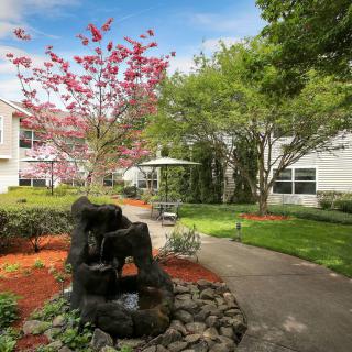 A beautifully landscaped garden with a stone fountain and meandering pathway on a sunny day.