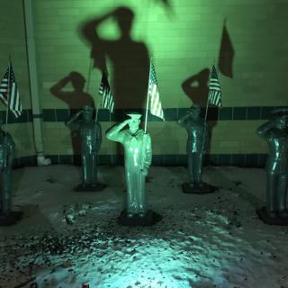 A group of statues saluting, illuminated by green lighting, with American flags in the background.