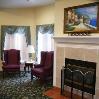A cozy living room featuring a fireplace, two armchairs, and a colorful painting above the mantel.