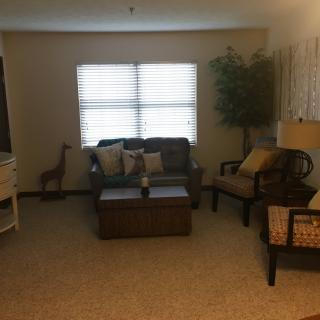 A cozy living room with sofas, armchairs, a coffee table, and a large window with curtains.