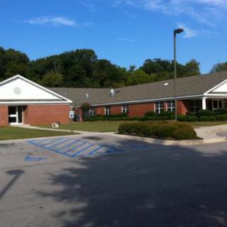 A suburban building with a parking lot and trees in the background under a blue sky.