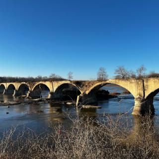 A scenic view of a historic bridge spanning a tranquil river under a clear blue sky.