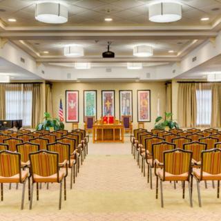 A well-lit conference room with rows of chairs facing a stage adorned with decorative art pieces.