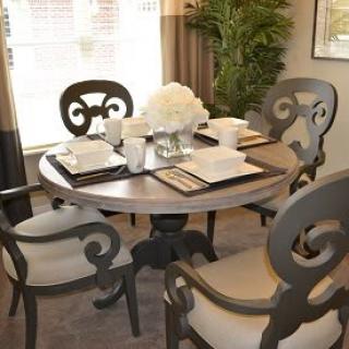 A stylish dining room with a round table set for four, adorned with elegant place settings and a centerpiece of white flowers.