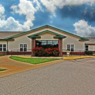 A front view of a single-story building with a well-maintained driveway and landscaping, set against a cloudy sky.