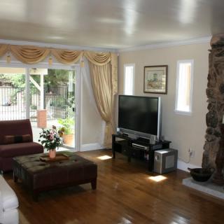 A cozy living room with a television, sofa, and fireplace, featuring hardwood floors and elegant curtains.