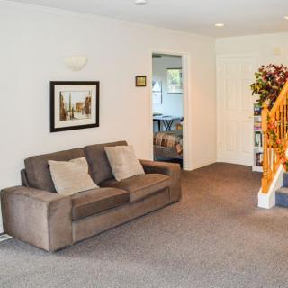 A cozy living room featuring a brown sofa, carpeted floor, artwork on the wall, and wooden stairs leading upstairs.