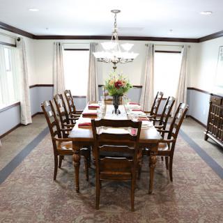 A spacious dining room featuring a large table surrounded by wooden chairs, adorned with a floral centerpiece and elegant lighting.