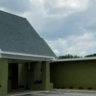 A green building with a sloped roof against a cloudy sky.