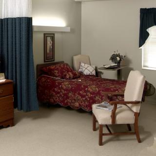 A cozy bedroom with a single bed, upholstered chair, and a small lamp by the window.