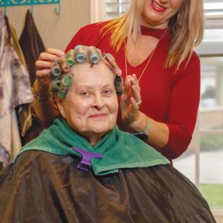 An older woman smiling while getting her hair styled with curlers at a salon.