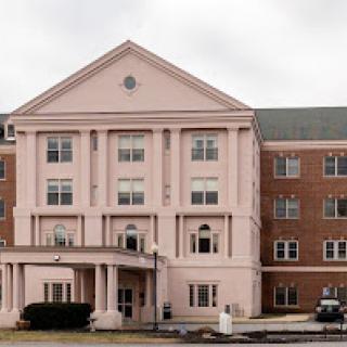 A beautiful pink residential building with a brick extension under a cloudy sky.