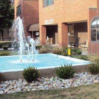 A tranquil outdoor scene featuring a decorative fountain in front of a brick building.