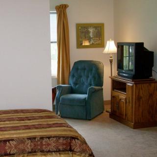 A cozy bedroom with a comfortable chair, television, and warm lighting.