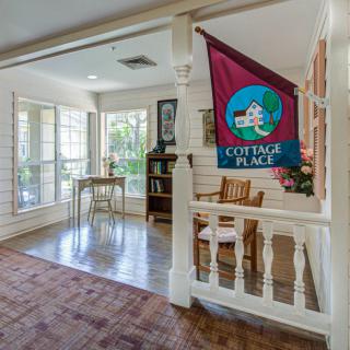 A cozy indoor space with a seating area and large windows, featuring a banner that reads 'Cottage Place'.