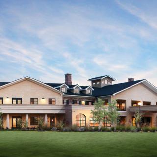 A large, luxurious mansion set against a blue sky with surrounding greenery.