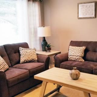 A cozy living room with dark sofas, a wooden coffee table, and a lamp by the window.