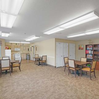 A spacious room with tables and chairs, featuring bright lighting and a small kitchen area.