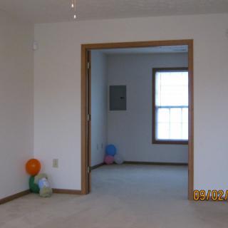 An empty room with a doorway leading to another room, featuring balloons on the floor and a window letting in natural light.