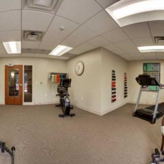A small fitness room with a treadmill, stationary bike, and weights.