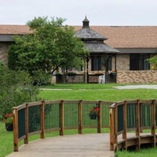 A wooden bridge leads to a brick building surrounded by greenery.