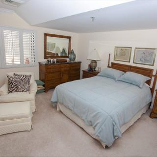 A cozy bedroom featuring a bed with blue bedding, an armchair, and a dresser adorned with decorative items.