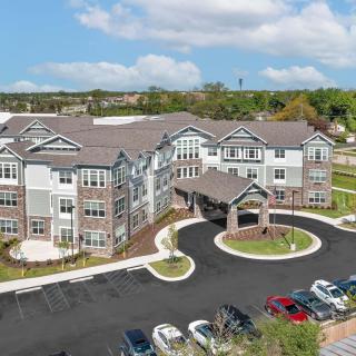 Aerial view of a modern residential building with a surrounding parking lot and landscaped areas under a partly cloudy sky.