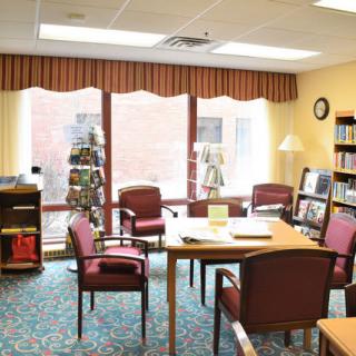 A cozy library reading room with bookshelves, table, and chairs.