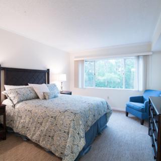 A cozy bedroom with a large window, featuring a bed and a blue armchair.