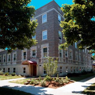 A brick residential building surrounded by trees on a sunny day.