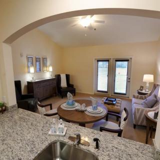 A modern open-concept living room and dining area viewed from the kitchen, featuring stylish furniture and a neatly set dining table.