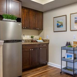 A cozy kitchen area in an apartment featuring wooden cabinets, a stainless steel refrigerator, and decorative artwork.