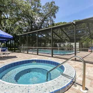 An outdoor area featuring a hot tub and a fenced pool, surrounded by trees.
