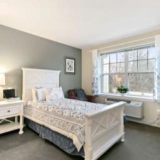 A cozy bedroom with a white bed, nightstand, and a large window.