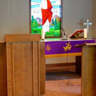 A church altar with a stained glass window depicting a religious scene.