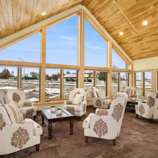 A cozy living room with large windows, wooden ceiling, and comfortable armchairs.