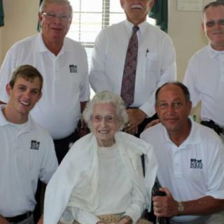 A group of men smiling and posing with an elderly woman indoors.