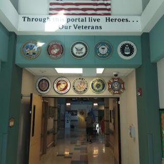 A tribute to veterans displayed at the entrance of a community center, featuring various military insignias and an American flag.