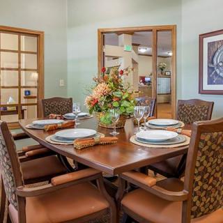 A cozy dining room with a wooden table set for four, featuring elegant plates and floral centerpiece.