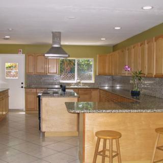 A modern kitchen with wooden cabinets and granite countertops, featuring an island with stools.