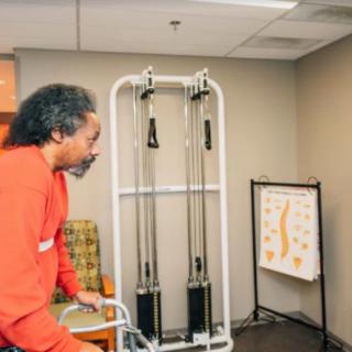 An elderly person using a walker in a rehabilitation room with exercise equipment.