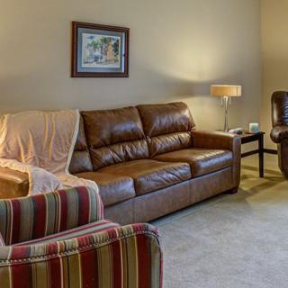 A cozy living room featuring a brown leather sofa, a striped armchair, and a standing lamp.