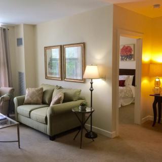 A cozy living room with elegant decor, featuring a comfortable sofa, lamps, and a view into an adjacent bedroom.