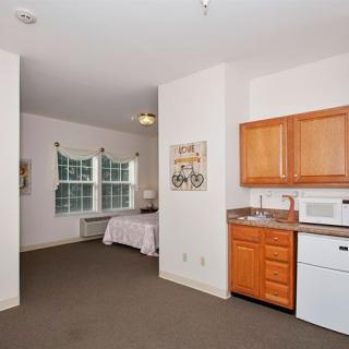 A cozy studio apartment featuring a kitchenette and bedroom area with natural lighting.