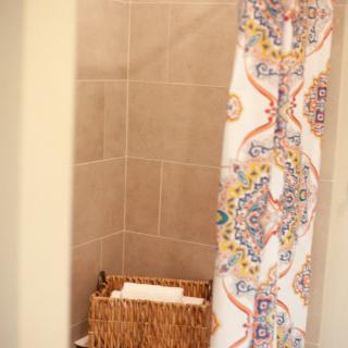 A bathroom shower area with a colorful patterned curtain and a wicker basket for storage.