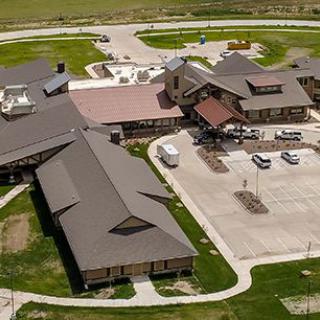 Aerial view of a building complex with a parking lot and surrounding greenery.