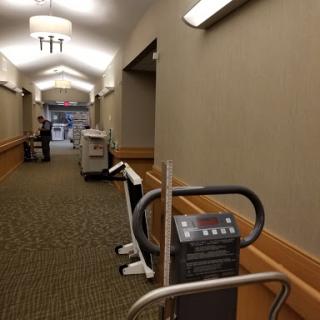 A view of a well-lit hallway featuring exercise equipment and carpet flooring.