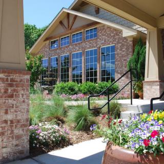 A beautifully landscaped brick building with large windows and colorful flowers in the foreground.
