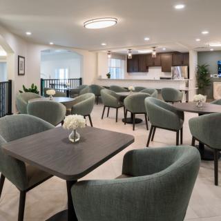 A modern dining area with several tables and chairs, adjacent to a kitchen with contemporary lighting.