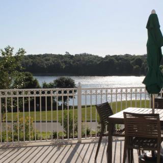 A serene lakeside view from a deck with outdoor seating and an umbrella.